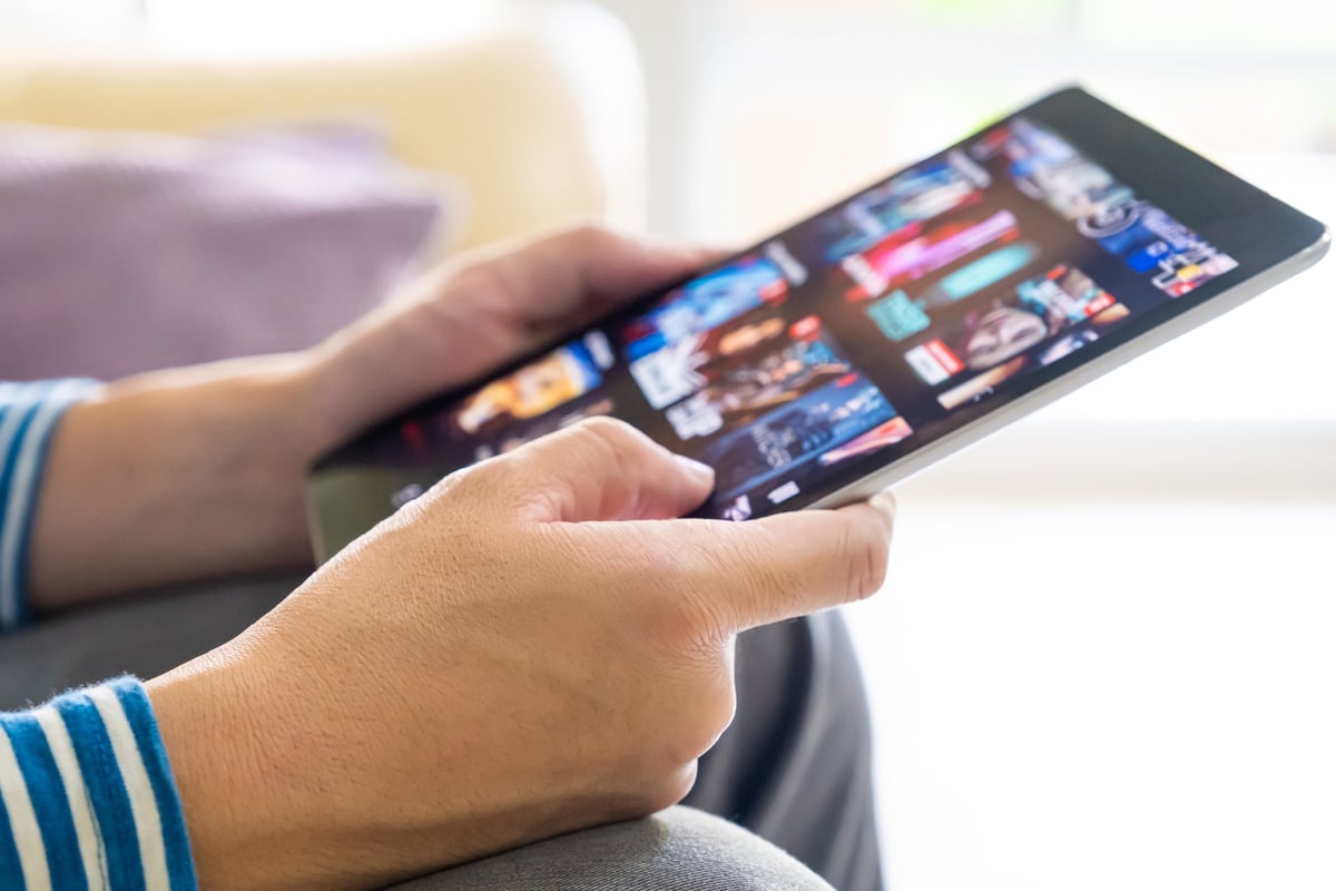 Person browsing a streaming app interface on a tablet while relaxing at home